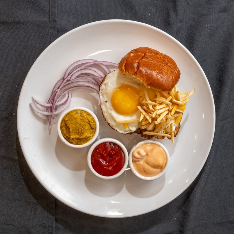 Zilus Essen's kosher burger with a fried egg, shoestring fries, red onions, and three dipping sauces.