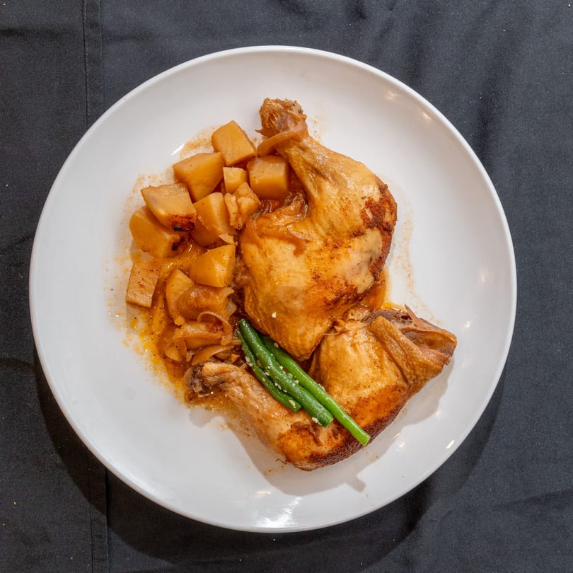 Two roasted chicken thighs with cubed potatoes and green beans on a white plate.