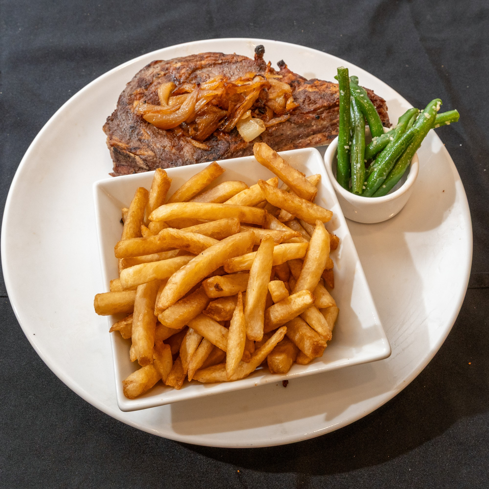 Grilled steak topped with caramelized onions, a side of golden french fries, and green beans.
