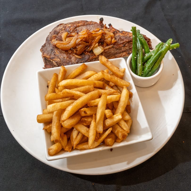 Grilled steak topped with caramelized onions, a side of golden french fries, and green beans.