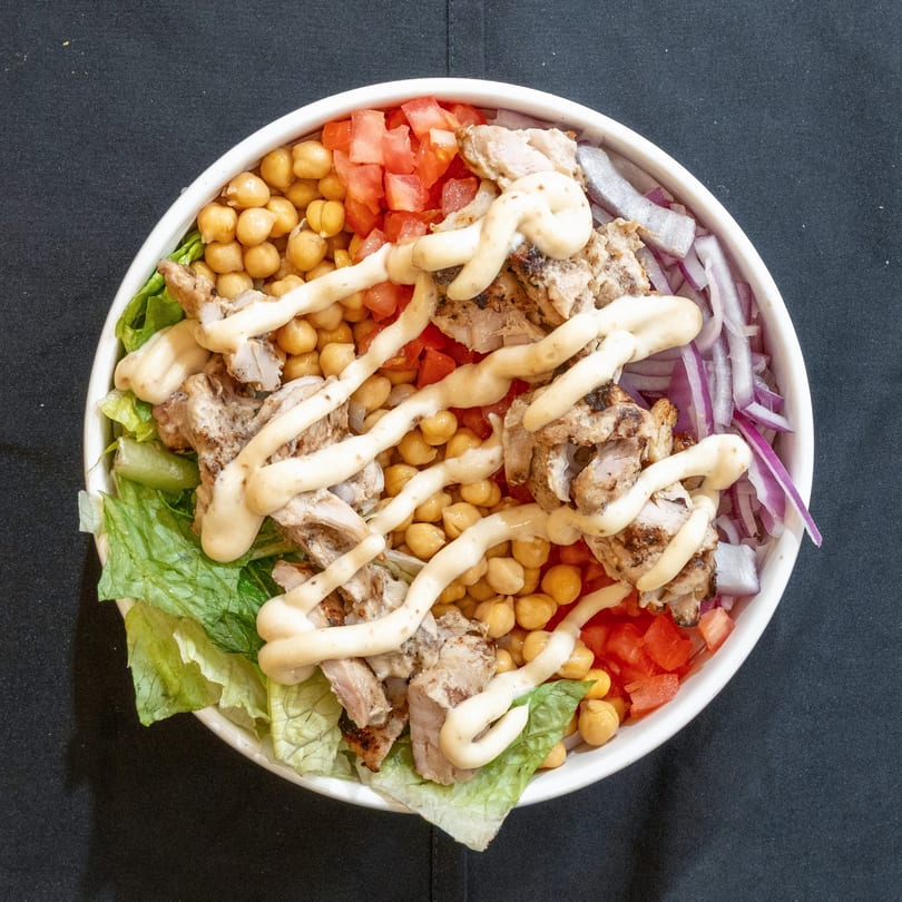 Overhead view of a Zilus Essen kosher chicken bowl with chickpeas, tomatoes, onions, and sauce.