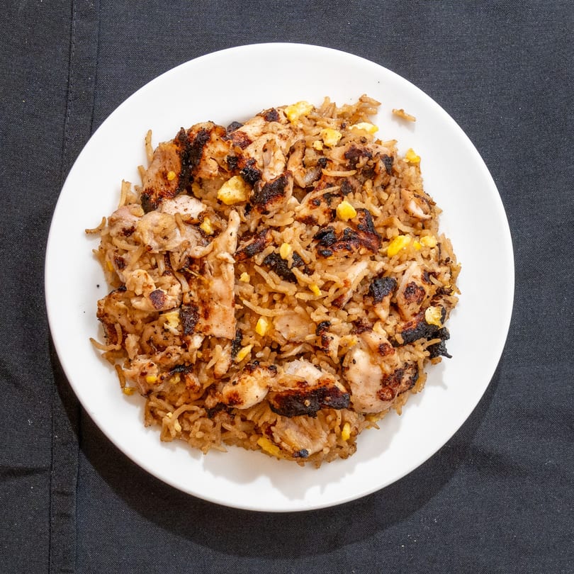 Zilus Essen's kosher chicken fried rice with charred chicken pieces and corn on a white plate.