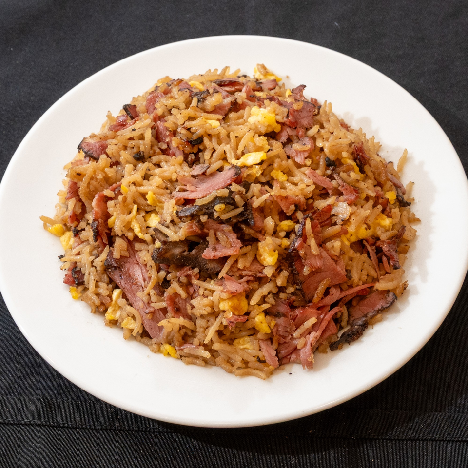 A white plate holds a generous serving of kosher pastrami fried rice with scrambled eggs.