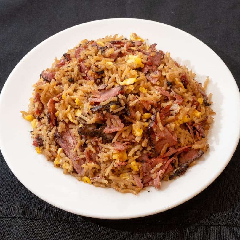 A white plate holds a generous serving of kosher pastrami fried rice with scrambled eggs.