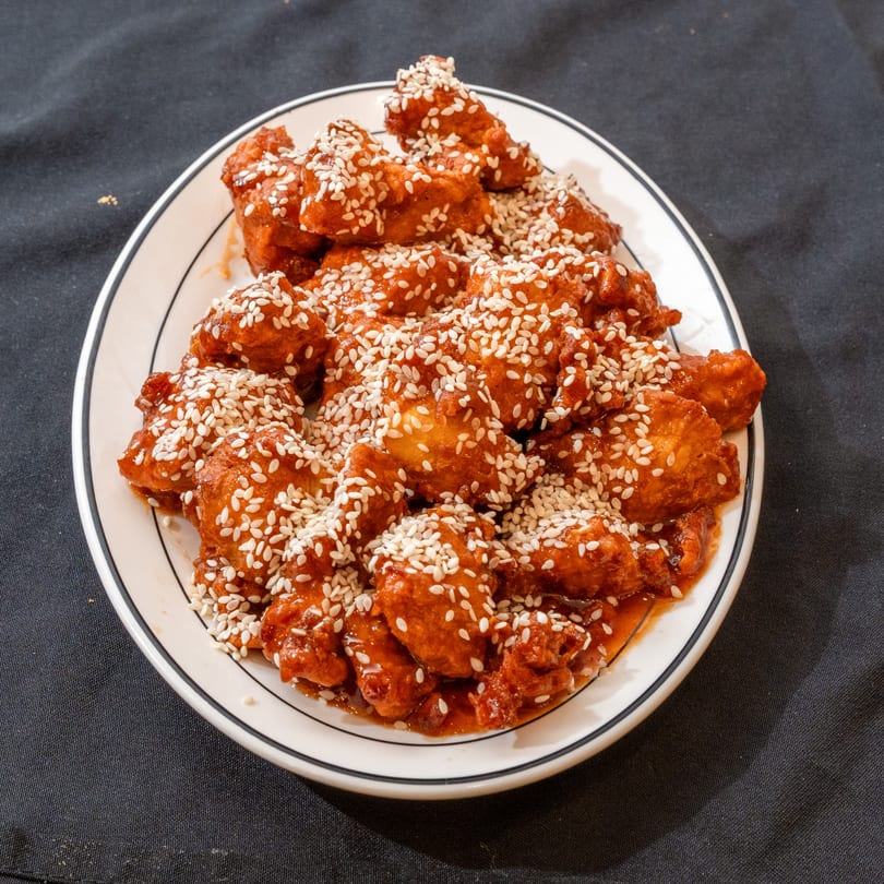A plate of Zilus Essen's kosher sesame chicken, glistening with sauce and topped with sesame seeds.