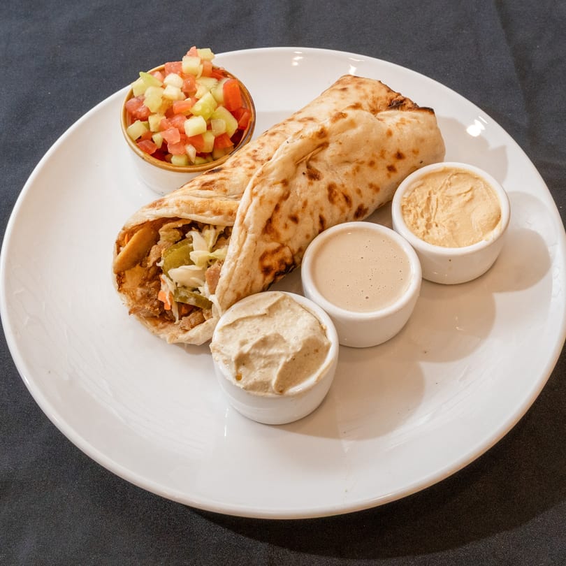 Kosher shawarma wrap with chopped salad, hummus, and tahini on a white plate.